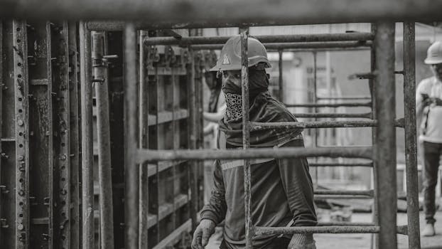 Black and white image of a construction worker wearing safety gear at a construction site.