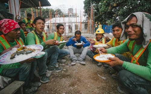 Group of People Eating while Sitting on Ground 