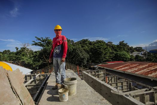 Construction worker standing on a building site with trees in the background under blue sky.