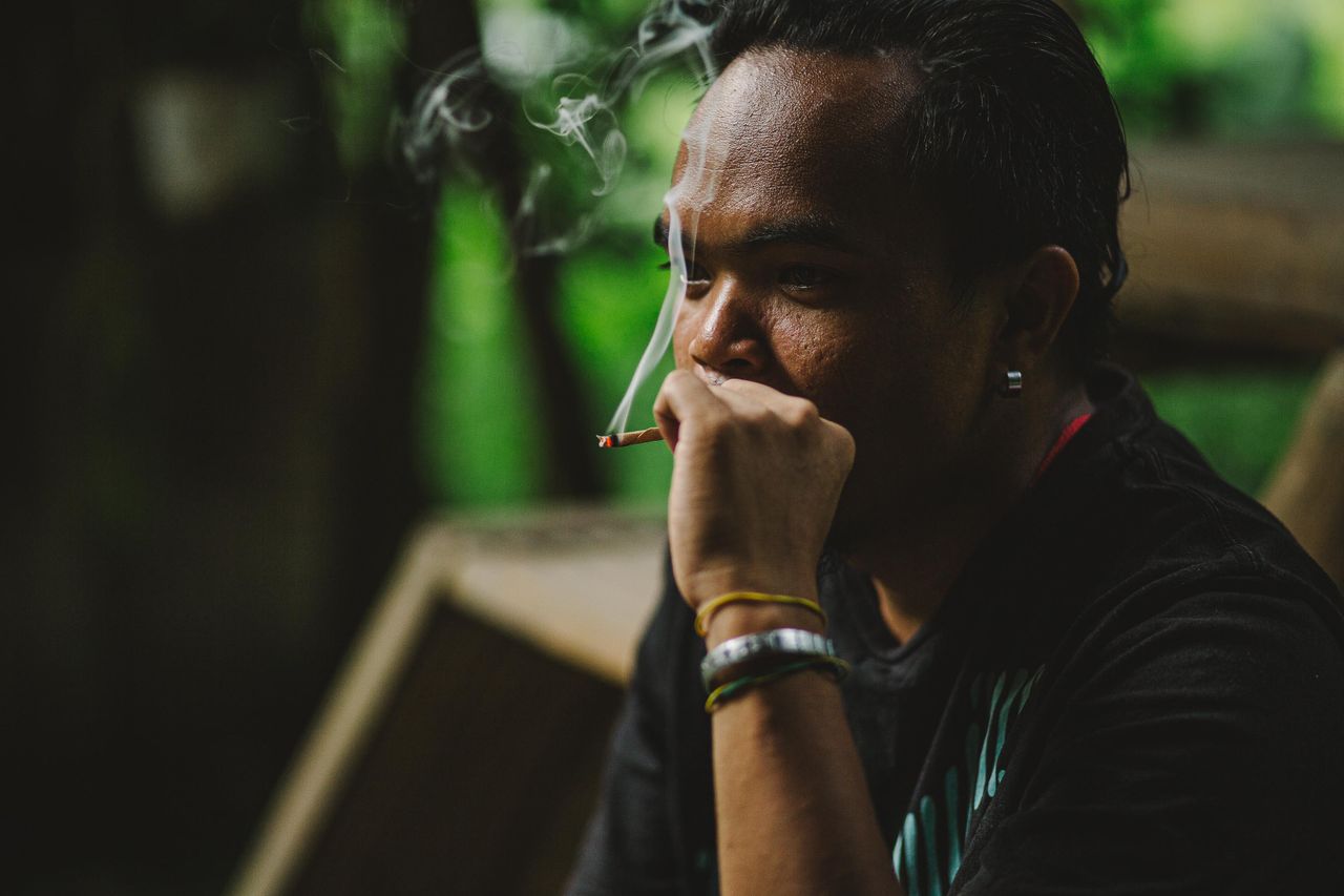 a contemplative man smoking a cigarette in a serene outdoor setting sm