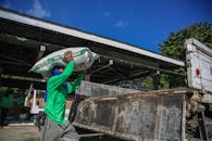 Man in Green Jumper Carrying White Bag on Head