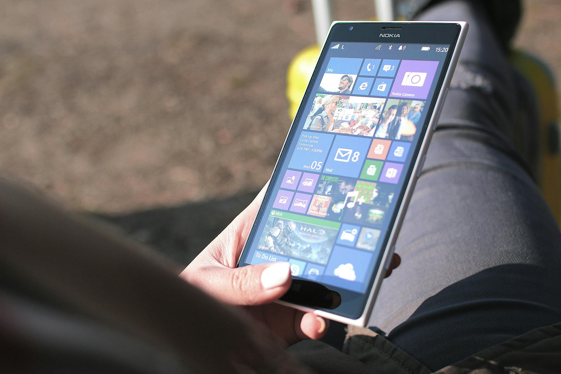 Close-up of a woman holding a Nokia smartphone running Windows operating system outdoors, showing touchscreen interface.