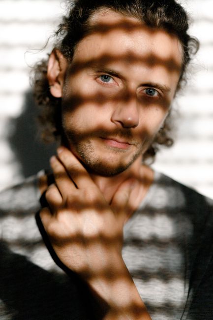 A thoughtful portrait of a man with striking lighting patterns casting shadows.