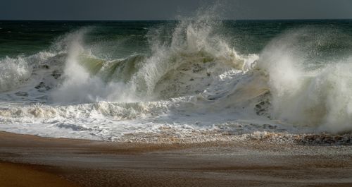 Free Powerful waves crash onto a sandy beach, capturing the dynamic and raw energy of the ocean. Stock Photo