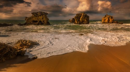 Free A breathtaking view of a rocky beach with waves crashing under a dramatic sunset sky. Stock Photo