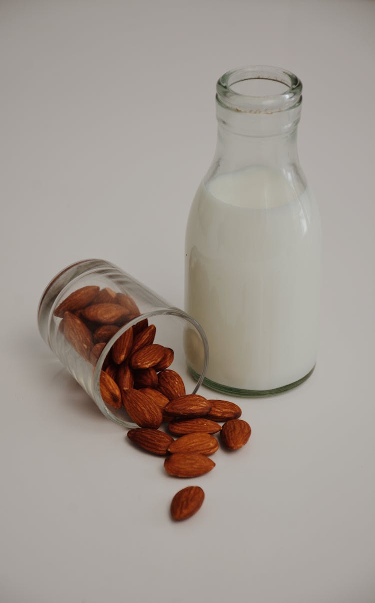 Bottle Of Milk Near Spilled Almonds On White Background