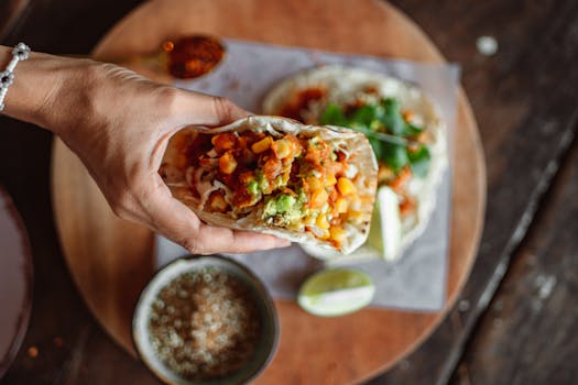 A hand holding a delicious Mexican taco filled with vibrant fresh ingredients on a wooden table.