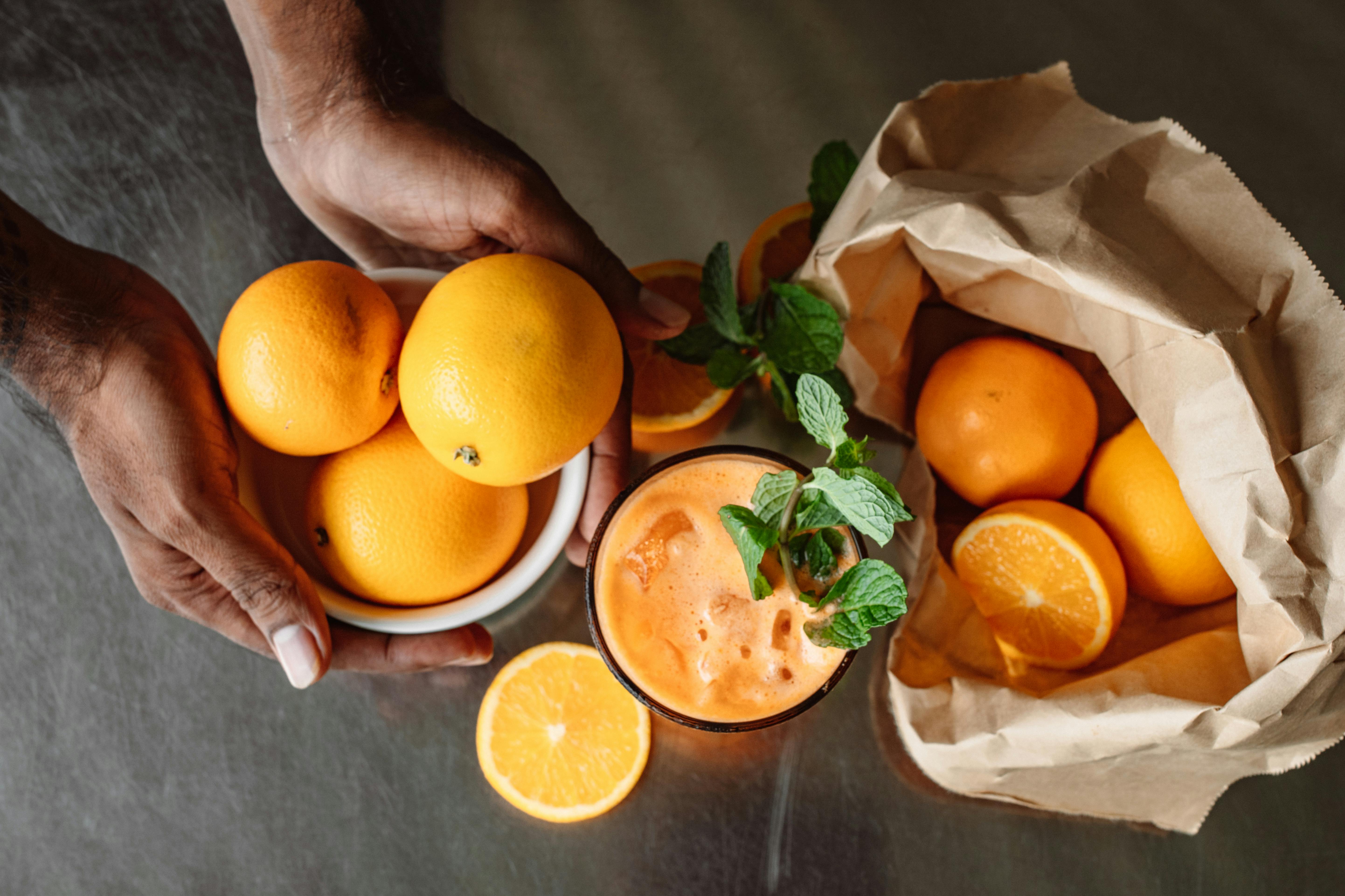 Top view of fresh orange juice with whole oranges and mint leaves.