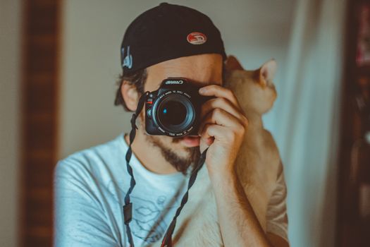 一个戴帽子的年轻人在室内抱着猫拍照