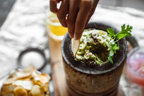 Free A woman's hand dipping a chip into fresh guacamole in a rustic bowl, showcasing delicious Mexican cuisine. Stock Photo