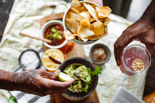 Three Unrecognizable Hands Holding Chips Lime and Cold Fruit Drink