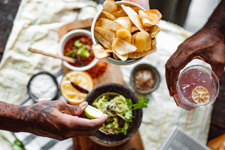 Three Unrecognizable Hands Holding Chips Lime And Cold Fruit Drink