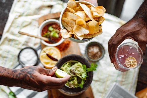 Free Hands holding chips and drink above a table with dips and guacamole, showcasing a vibrant food setup. Stock Photo