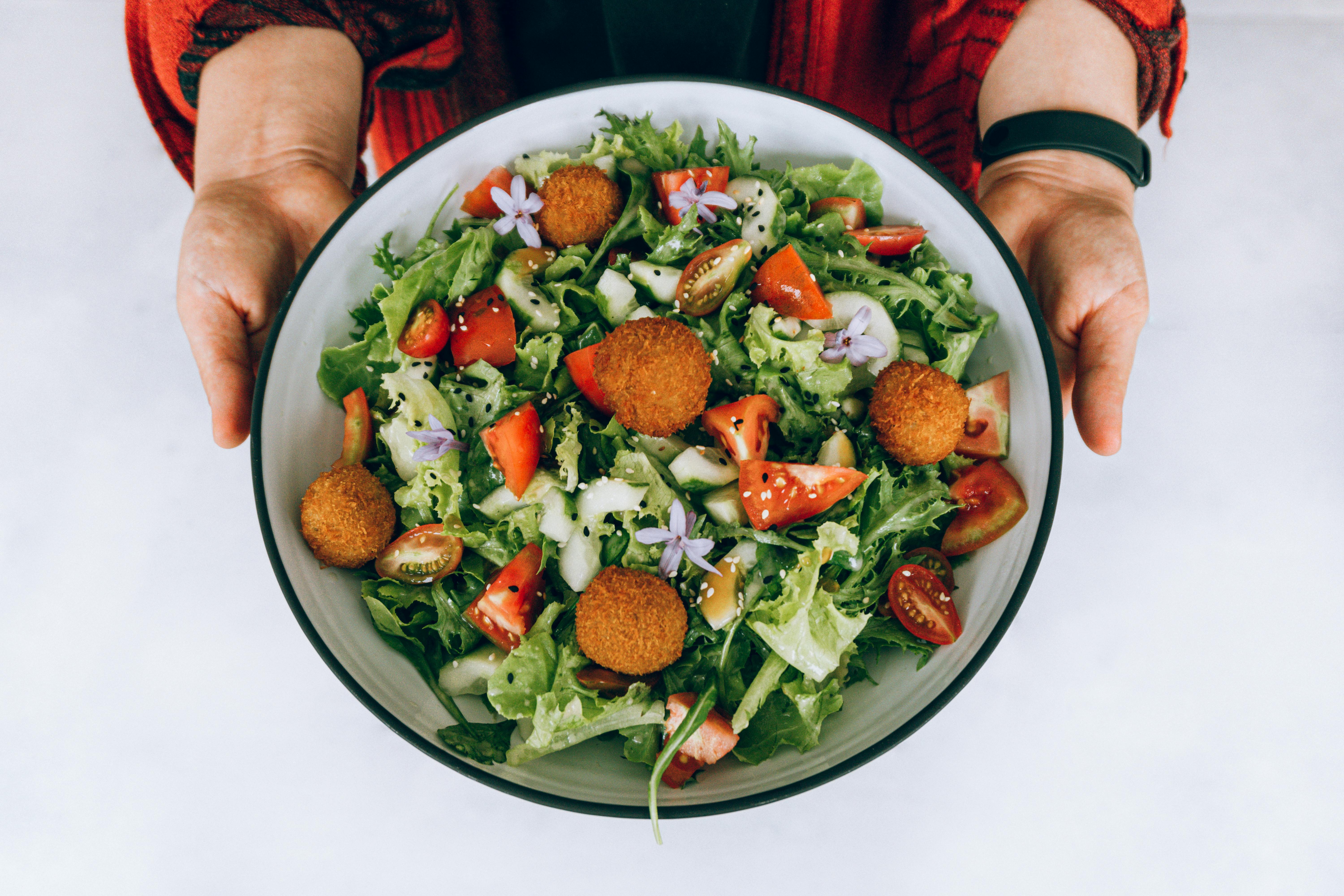 A vibrant fresh salad with crispy falafel, tomatoes, cucumbers, and purple flowers.