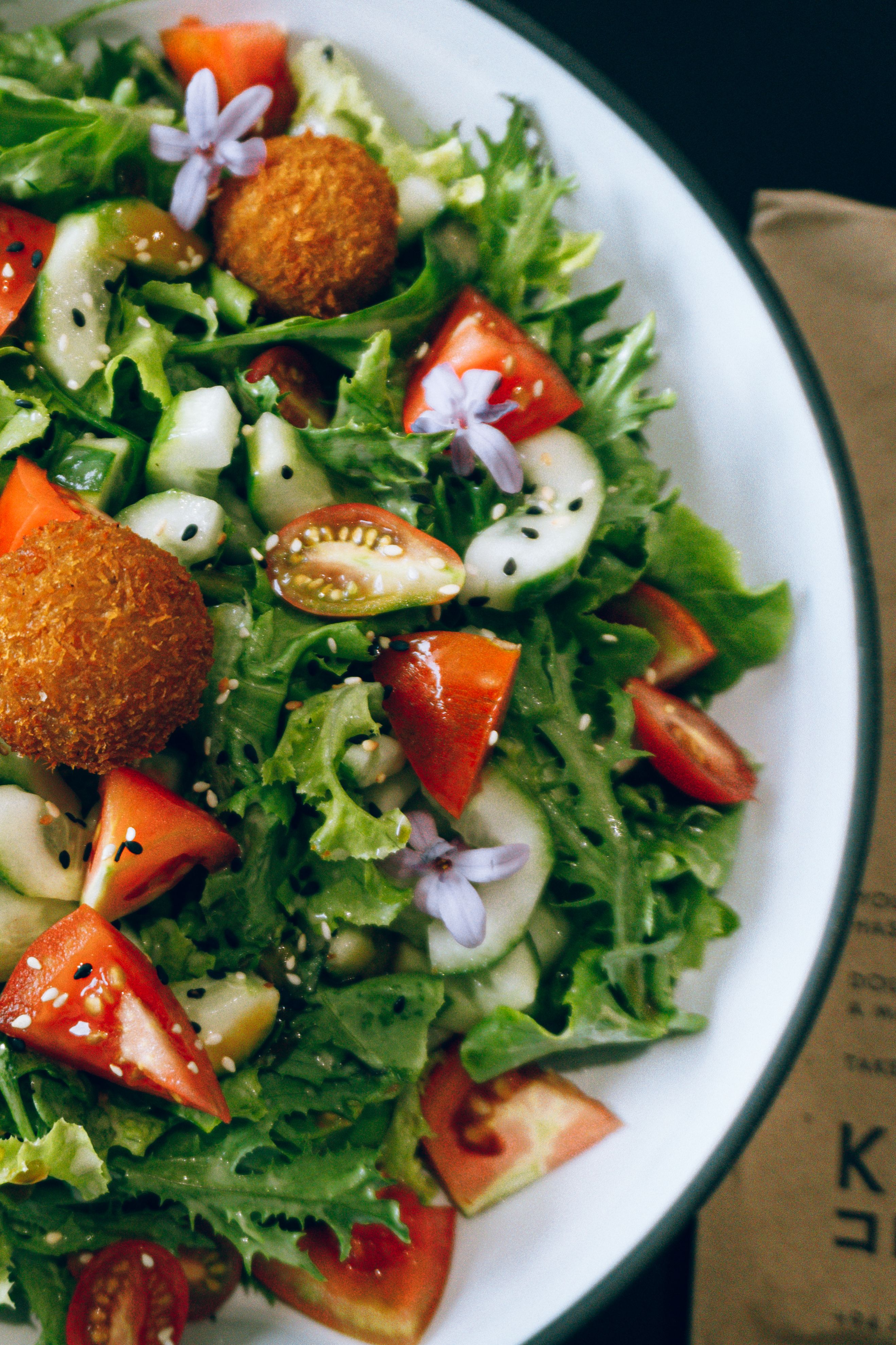 Colorful salad with fresh tomatoes, lentil balls, and edible flowers in a bowl.