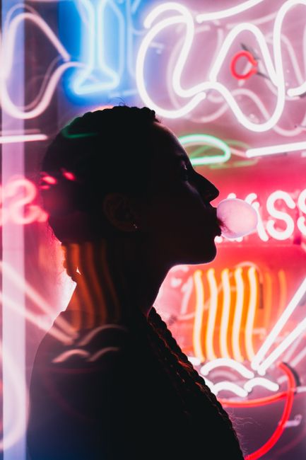 Silhouette of a woman blowing bubble gum in front of colorful neon lights, creating a vibrant and modern atmosphere.
