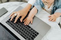 妈妈把宝宝的手和自己的手一起放在笔记本电脑键盘上，平衡育儿与工作