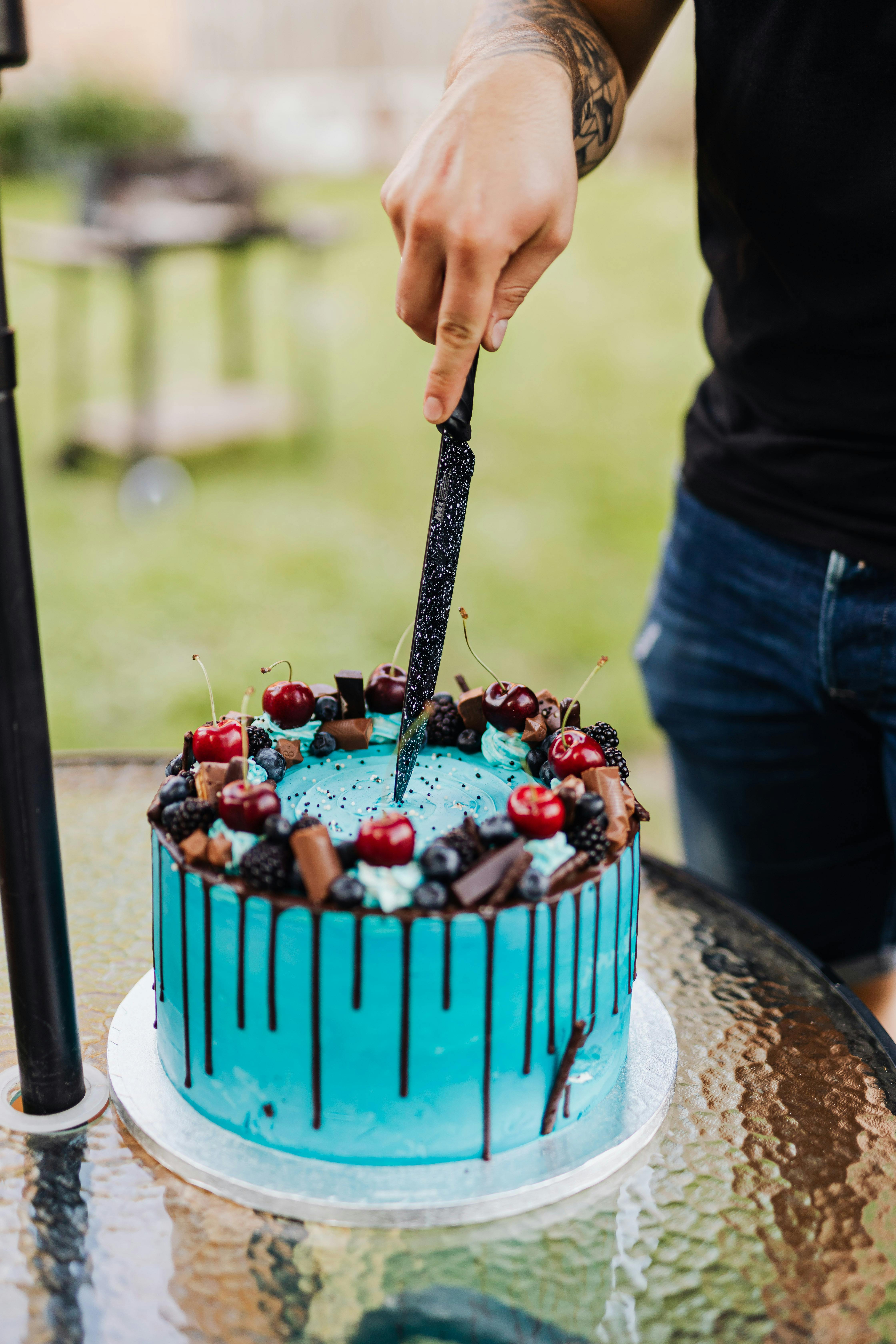 A vibrant blue birthday cake being sliced outdoors. Perfect for celebrations.