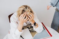 一个穿着白衬衫的女人沮丧地坐着，双手抱头，被工作任务压垮了