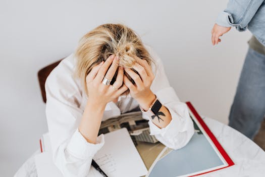 Frustrated woman in white shirt sitting with head in hands, overwhelmed by work tasks.