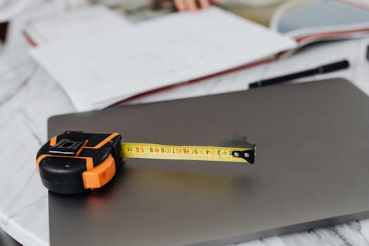 Close-up image of a measuring tape and a laptop on a work desk, representing precision in work.
