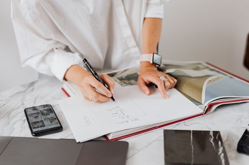 Free Close-up of hands writing notes at a desk with a smartphone and open book in an office. Stock Photo