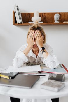 一名妇女不知所措地坐在家庭办公桌前，双手捂着脸，显得既压力重重又沮丧万分