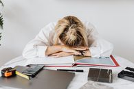 疲惫的女人穿着白衬衫，将头靠在摆满工作材料的桌子上