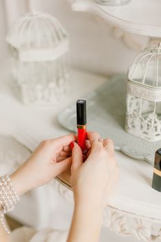 一位修剪着红色指甲、手腕戴着珍珠手镯的农妇坐在白色桌子前，手里拿着红色唇彩