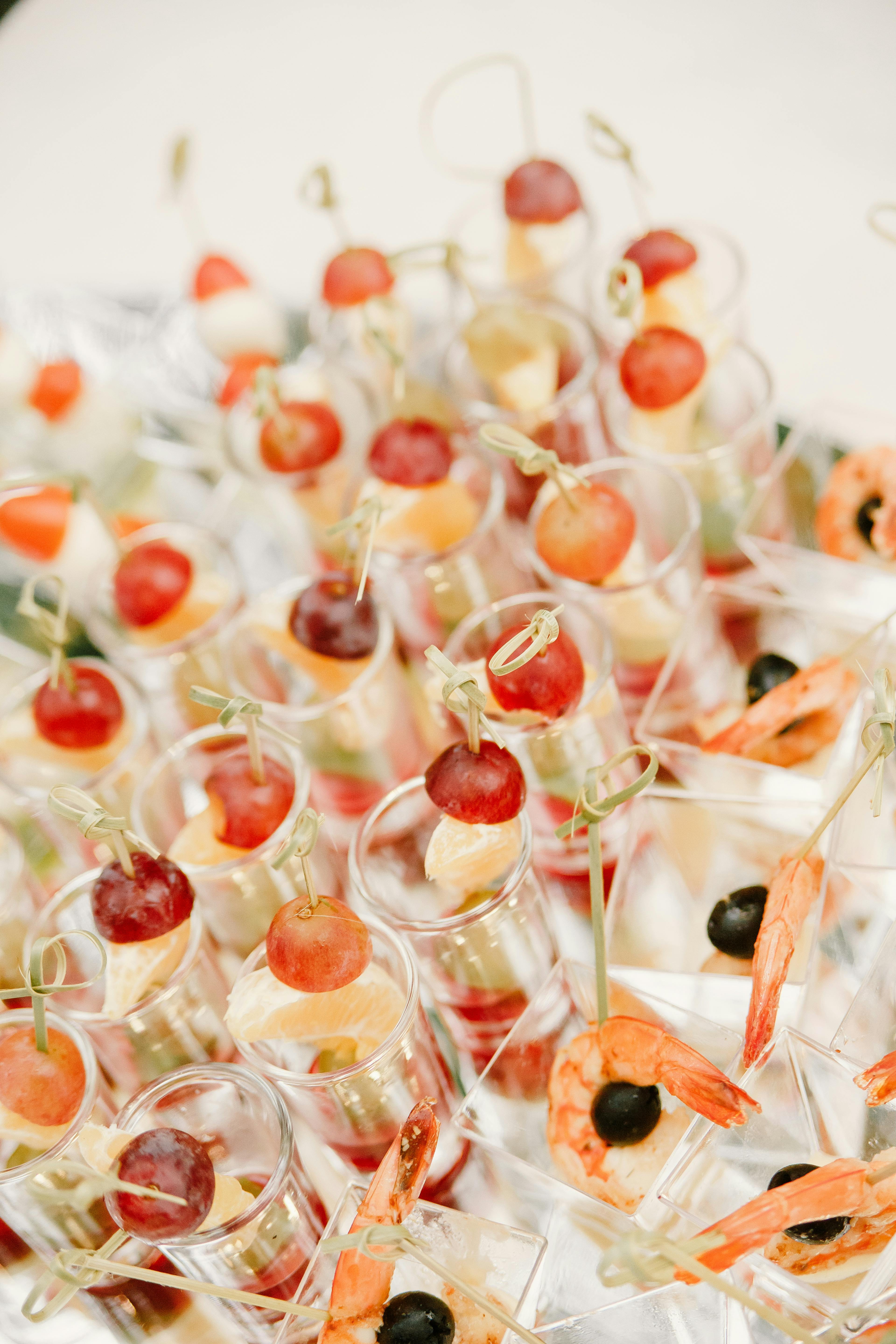 From above of rows of appetizers with grapes and shrimps in glassware served on white table