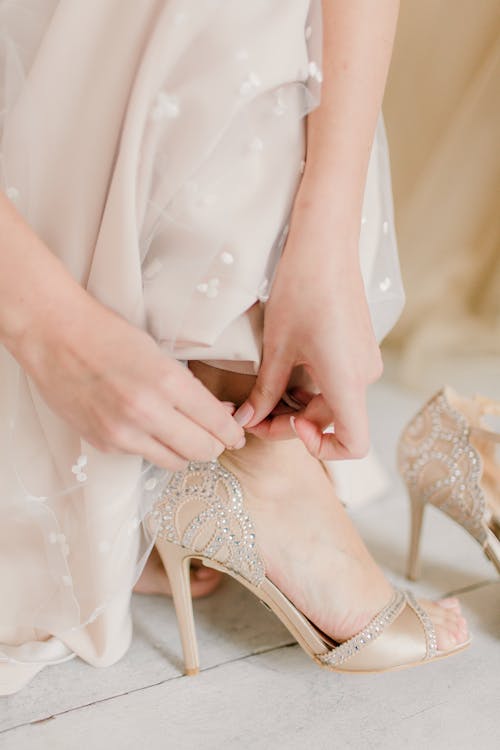 Crop anonymous woman in wedding dress putting high heeled shoes while preparing for wedding ceremony