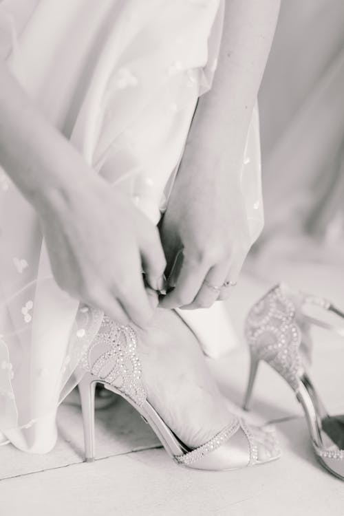 Free Black and white crop anonymous bride wearing elegant wedding dress and putting high heels before event Stock Photo