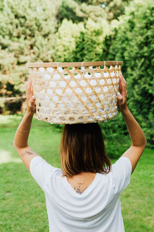 Free Woman holding a woven laundry basket on her head in a sunny outdoor setting. Stock Photo