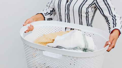 A close-up of a woman holding a white laundry basket filled with fresh, clean clothes.
