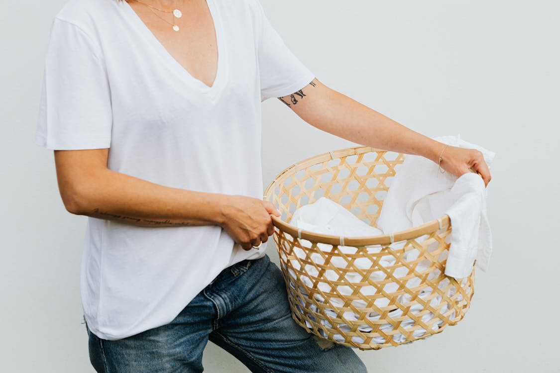 Free Woman in White V Neck Shirt and Blue Denim Jeans Holding Brown and White Woven Basket Stock Photo