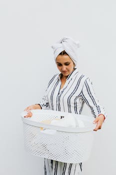 A woman in pajamas with a towel on her head holding a laundry basket, evoking a sense of relaxed home chores.