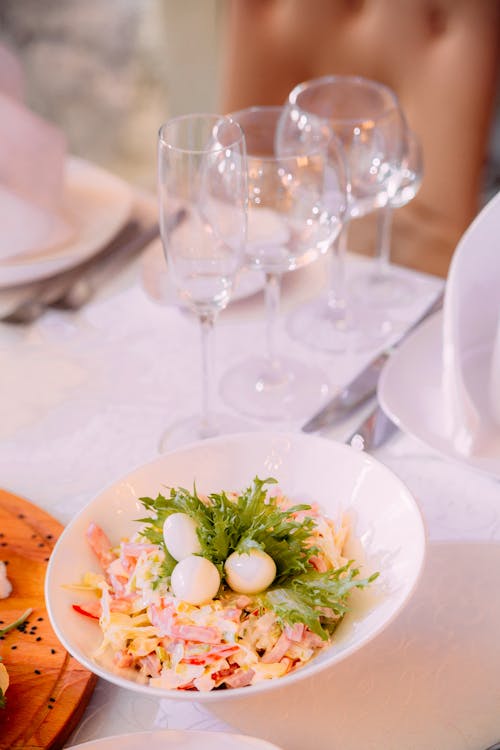From above of delicious appetizing salad decorated with green herbs in ceramic plate on table with glass dishes