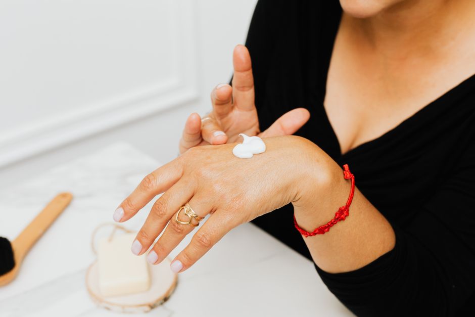 Close-up of a woman applying moisturizing cream to her hands as part of her skincare routine.