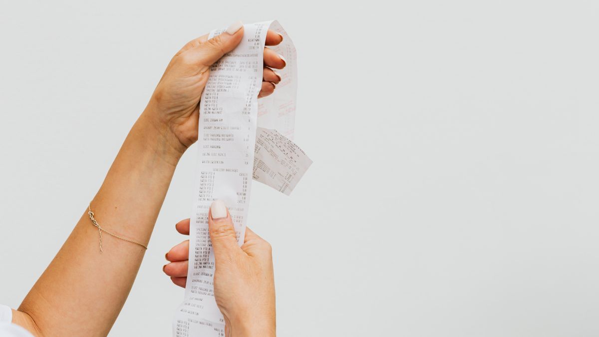 A detailed view of a person holding a long shopping receipt against a plain background.