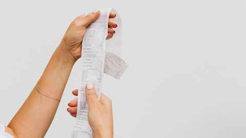 A detailed view of a person holding a long shopping receipt against a plain background.