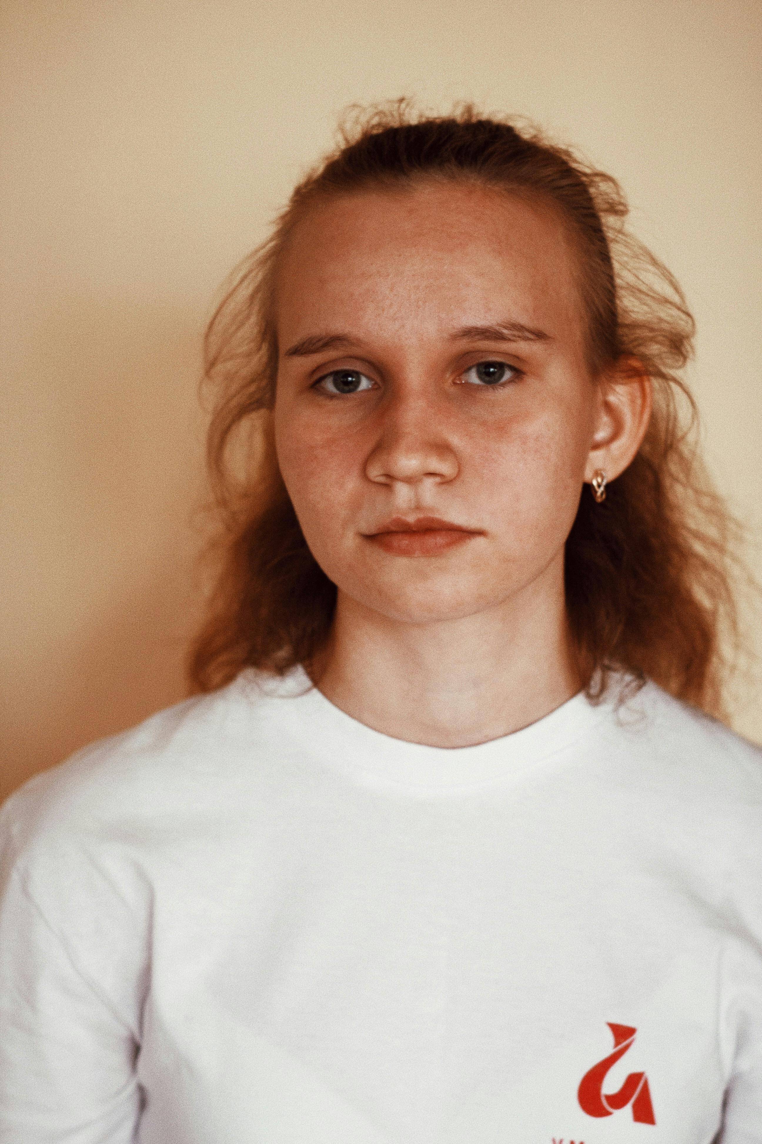 A close-up portrait of a thoughtful teenage girl wearing a white t-shirt. Neutral background.