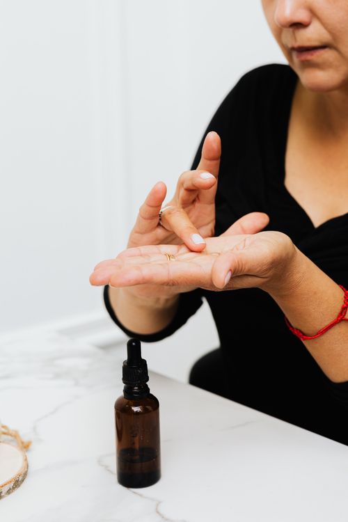 Free Close-up of a woman applying a skincare serum from an amber bottle on a marble surface. Stock Photo