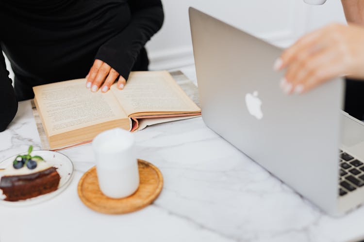 Hands Of Persons On An Open Book And A Laptop