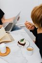 两个人在室内一边用笔记本电脑工作，一边享用甜点和咖啡