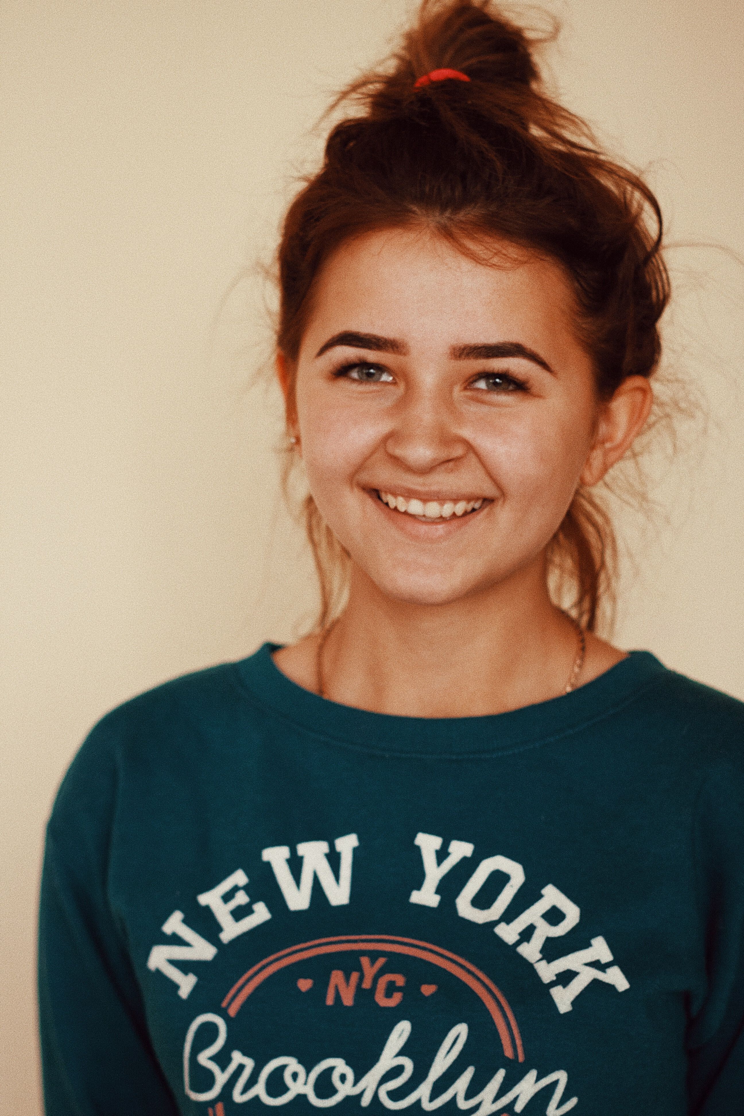 Casual portrait of smiling young woman in Brooklyn shirt with hair bun.