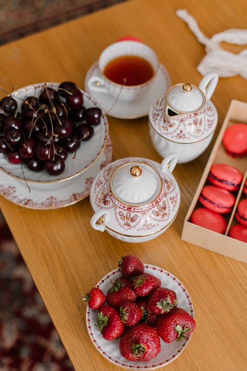 Free From above of delicious sweet macaroons served with plates of strawberries and cherries placed near tea in ceramic dish Stock Photo