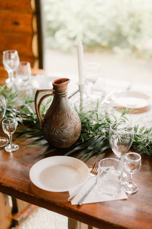 From above of elegant served table with glasses and tableware near green tropical plant against window