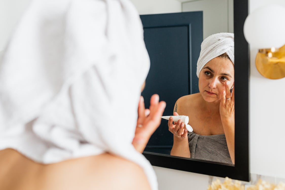 Free Mirror Reflection of a Woman Applying Face Cream Stock Photo