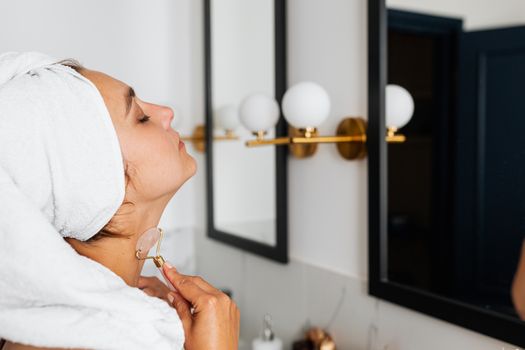 Young woman using a quartz face roller for self-care routine in a modern bathroom.