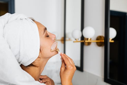 Free Woman Wearing a Head Towel Using a Face Roller Stock Photo